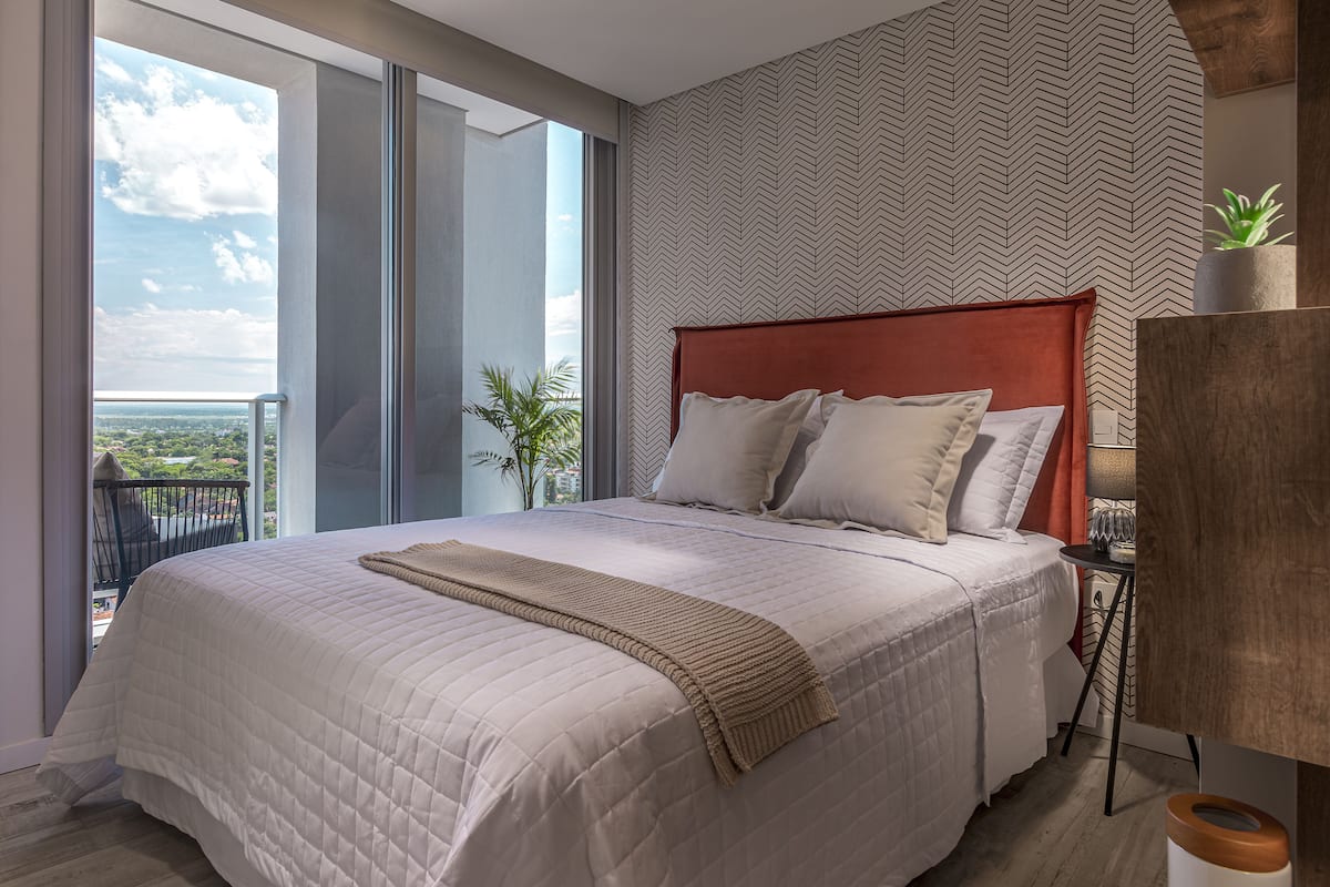 A modern bedroom with a large bed, a view of the outdoors, and a patterned wall.