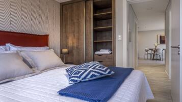 A neatly made bed with a patterned pillow, a blue blanket, and a wooden wardrobe in the background.