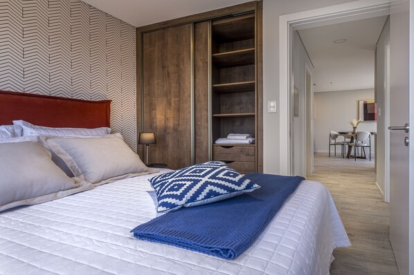 A neatly made bed with a patterned pillow, a blue blanket, and a wooden wardrobe in the background.