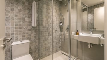 Un baño moderno con ducha de vidrio, inodoro y lavamanos con espejo.
