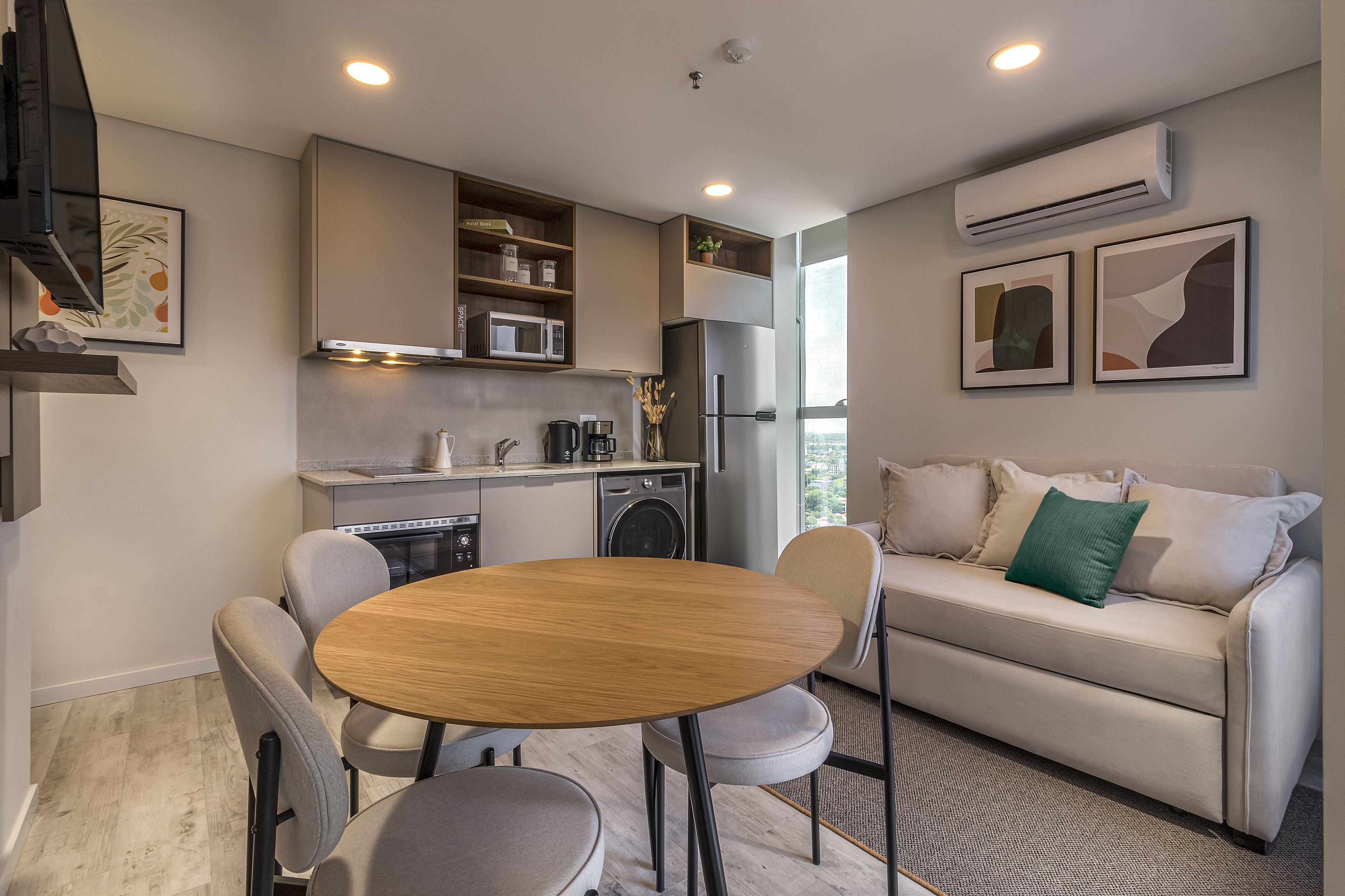 A modern kitchen with built-in appliances, a dining area with a round table, and a sofa with a green pillow.