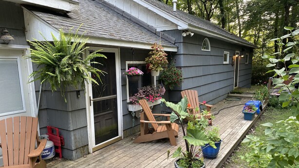 A wooden deck with two Adirondack chairs, a potted plant, and a small table. - Delightful cottage with huge yard on heavily wooded one acre lot in Union Pier. (Union Pier)