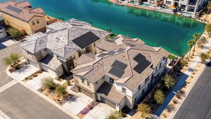 A residential area with houses featuring sloped roofs and solar panels, a clear blue water body, and a well-maintained landscape.