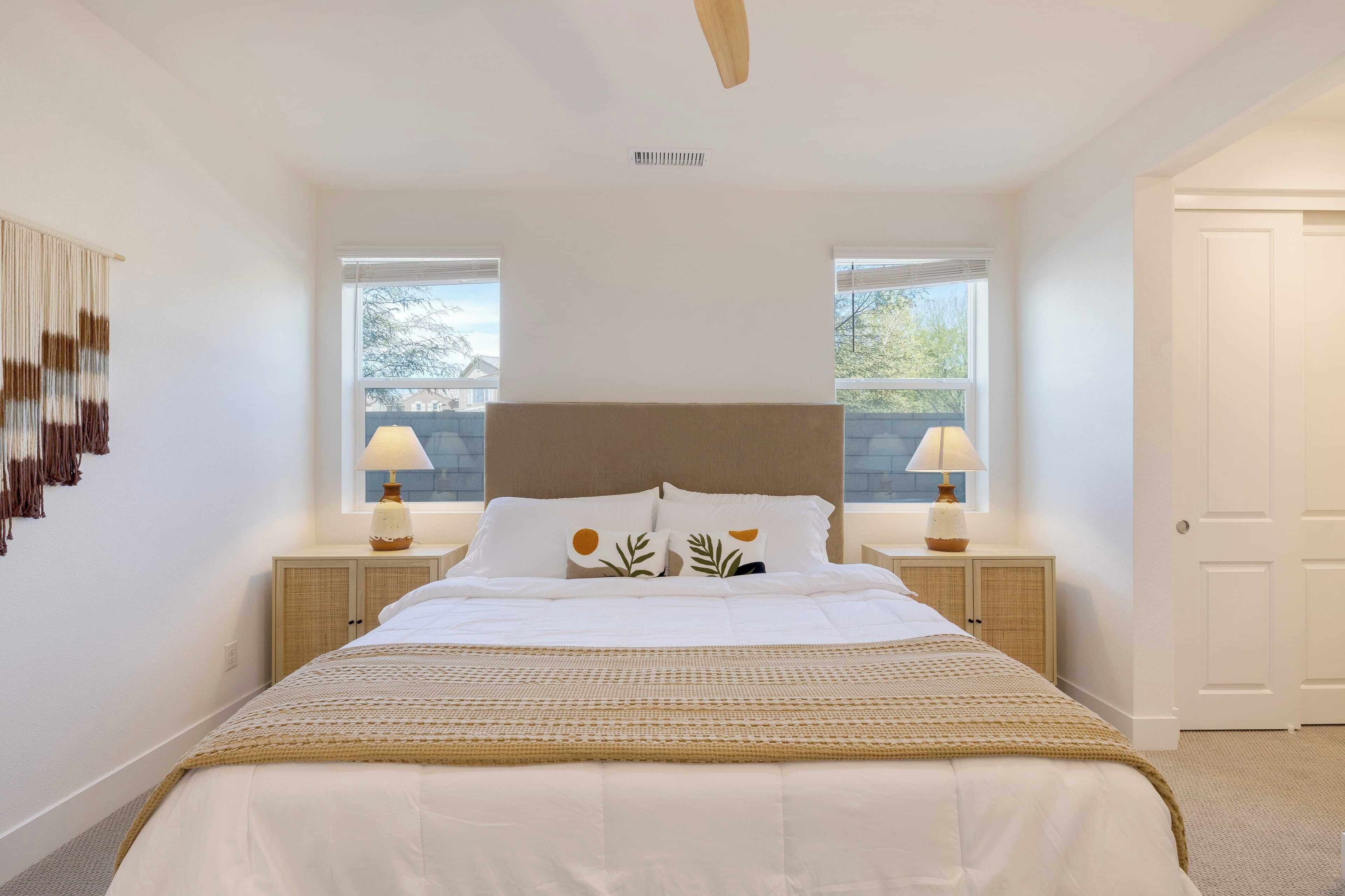 A bedroom with a large bed, two bedside tables with lamps, a headboard, and a view through the windows.