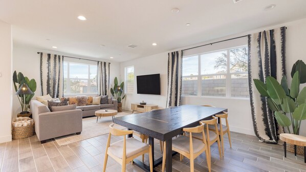 A modern living room with a sofa, coffee table, and dining area with chairs. - Lakefront w/ Private Pool, Great for Festival Season Lago Luxe by Avantstay (Indio)