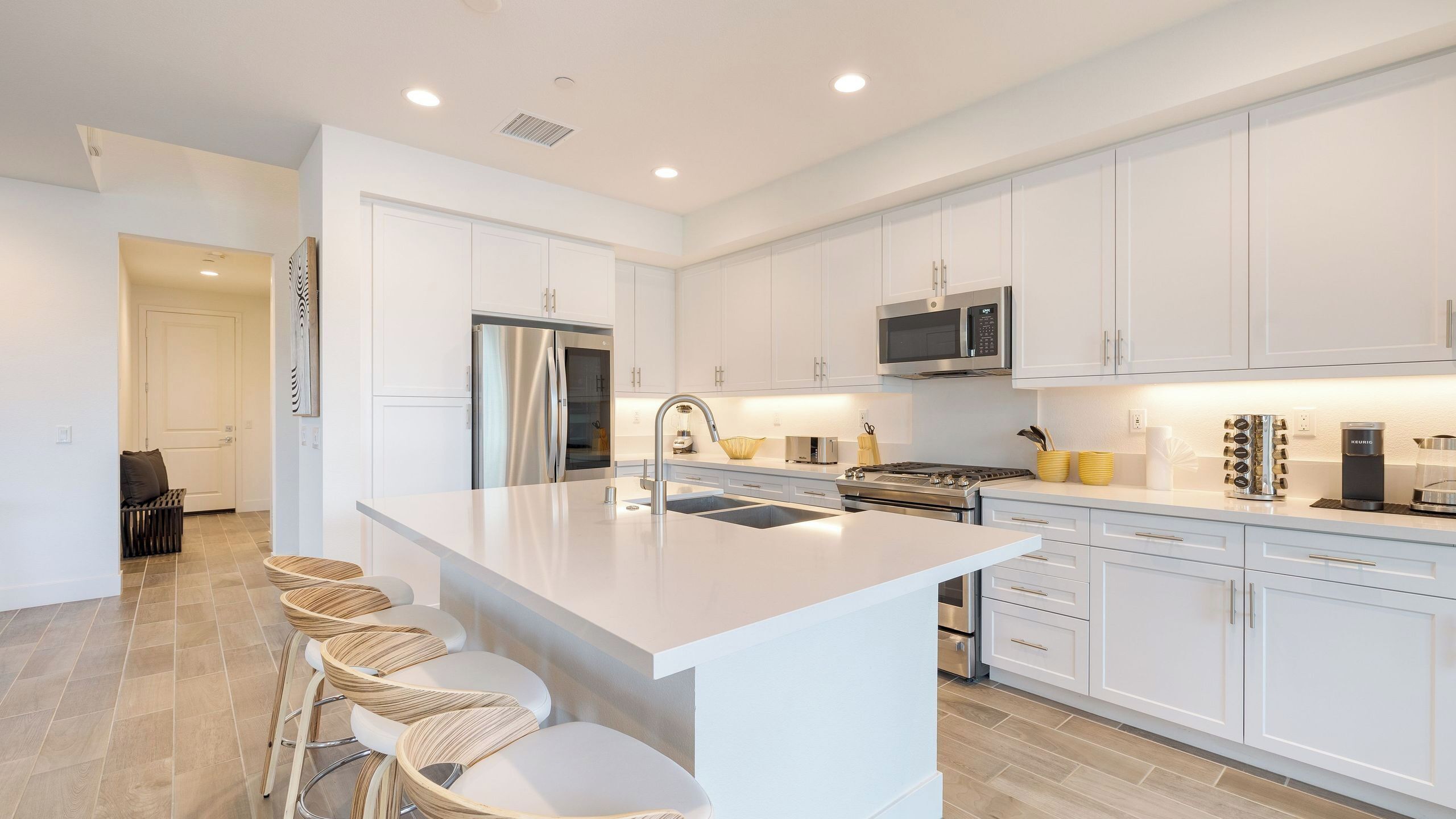 A modern kitchen with white cabinetry, stainless steel appliances, and a central island with bar stools.