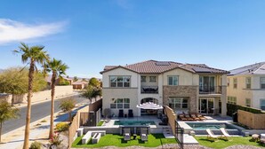 A two-story house with a swimming pool, outdoor seating, and a well-maintained lawn.