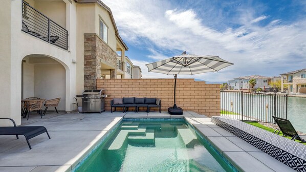Una piscina con zona de patio, mobiliario exterior y vista a un cuerpo de agua.