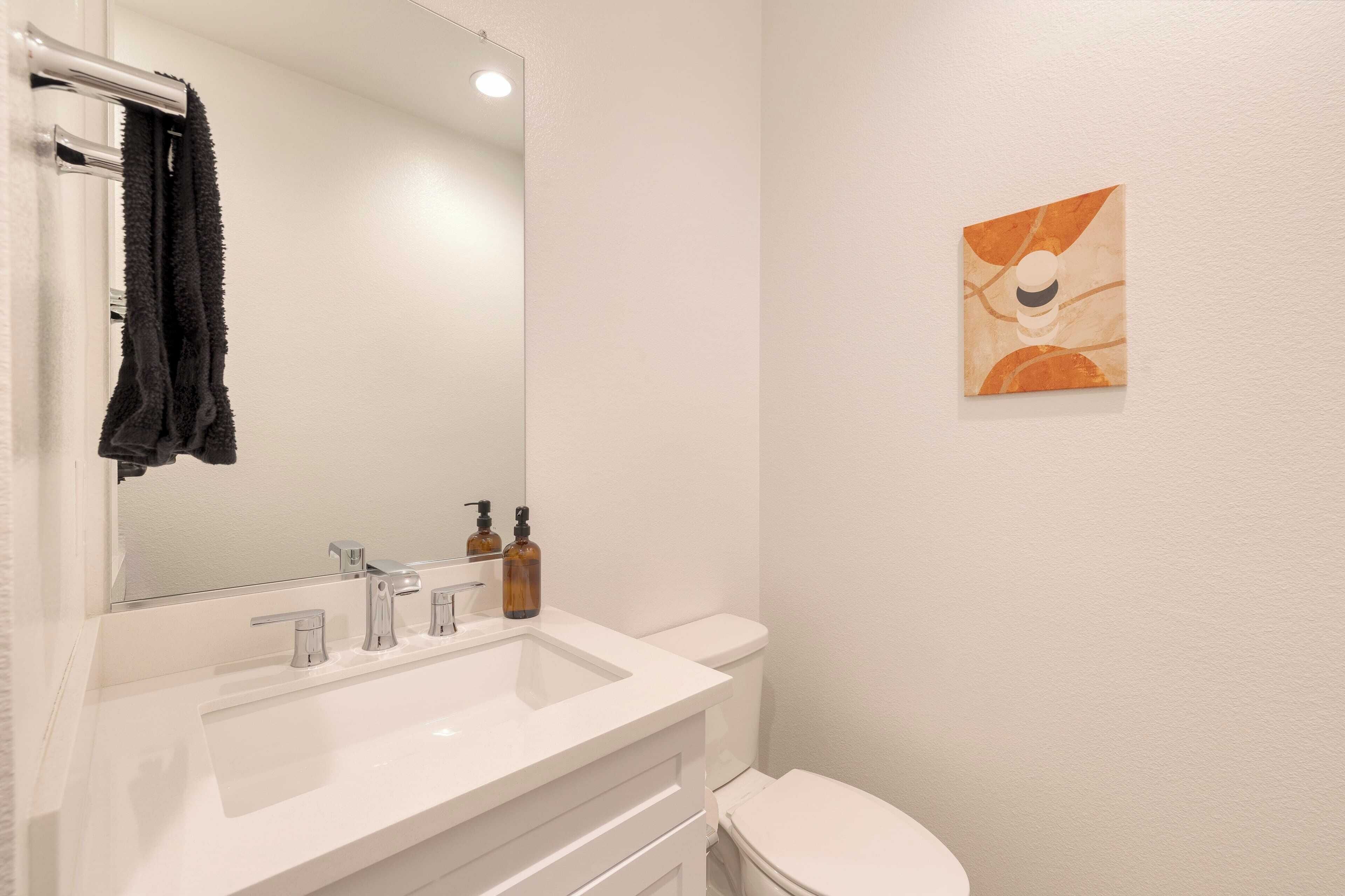 A bathroom with a white sink, a mirror, a towel rack, a toilet, and a wall-mounted artwork.