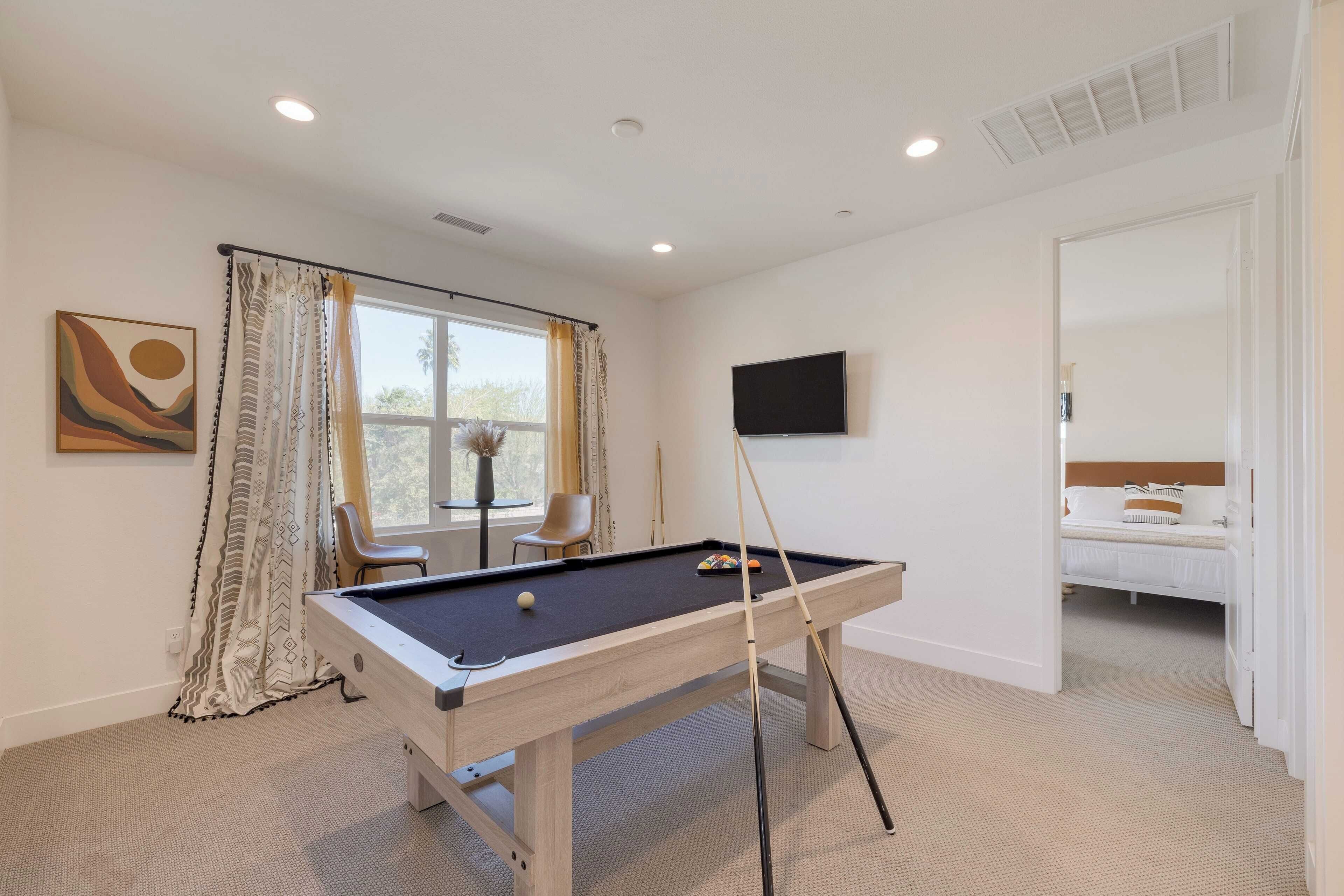Une table de billard dans une pièce où se trouvent un lit, un téléviseur et un tableau accroché au mur.