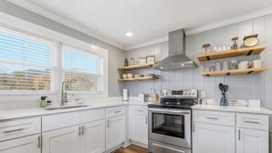 A modern kitchen with white cabinetry, a stainless steel oven, and wooden shelves above the counter. - Charming farmhouse in tranquil Candler, pet friendly w/fully fenced yard (Candler)