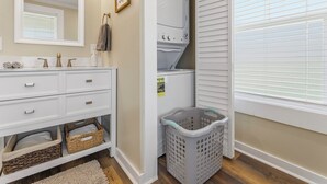 A bathroom with a white vanity, a mirror, a towel rack, a laundry basket, and a window with blinds. - Charming farmhouse in tranquil Candler, pet friendly w/fully fenced yard (Candler)