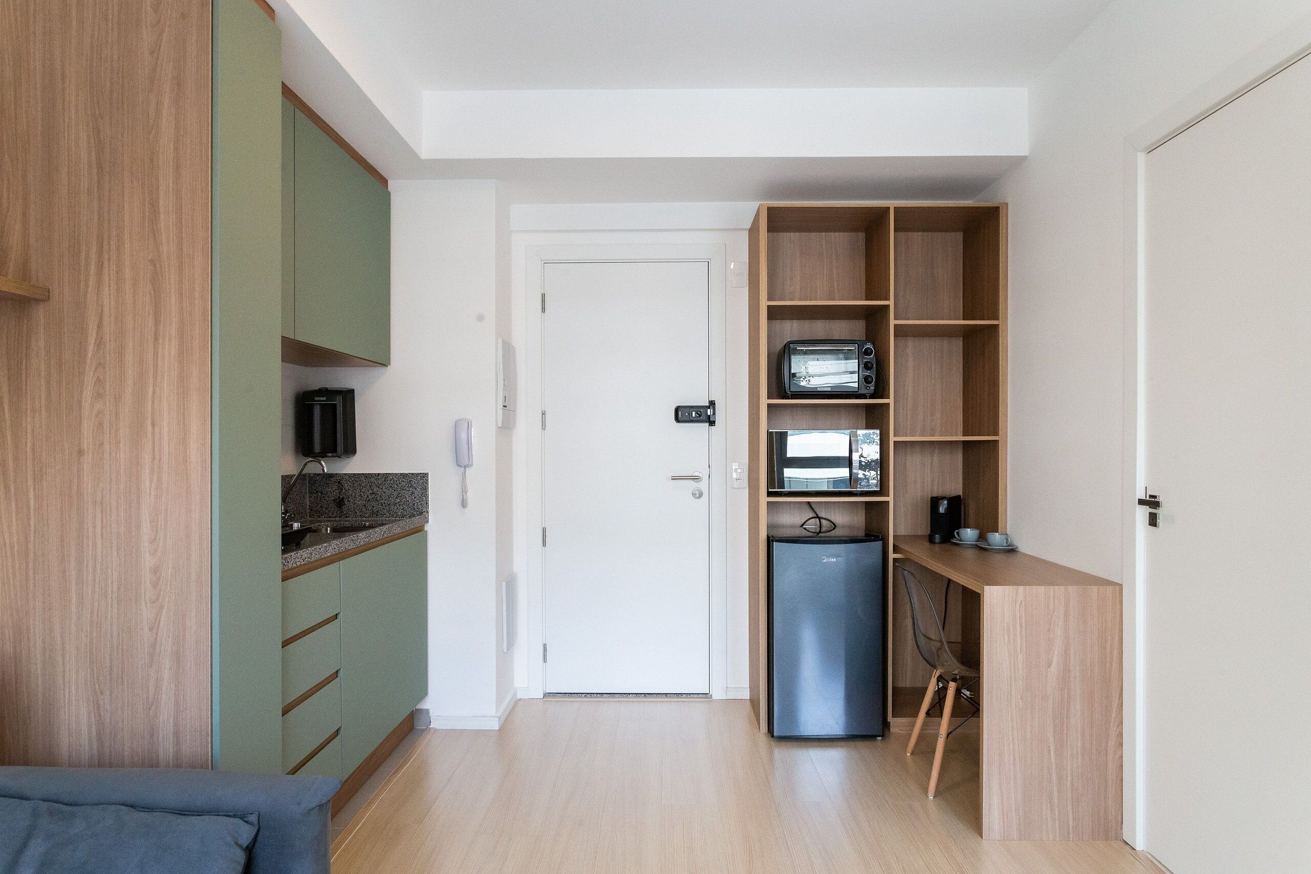 Een compacte keuken met een ingebouwde magnetron, een kleine koelkast en een houten schapunit.