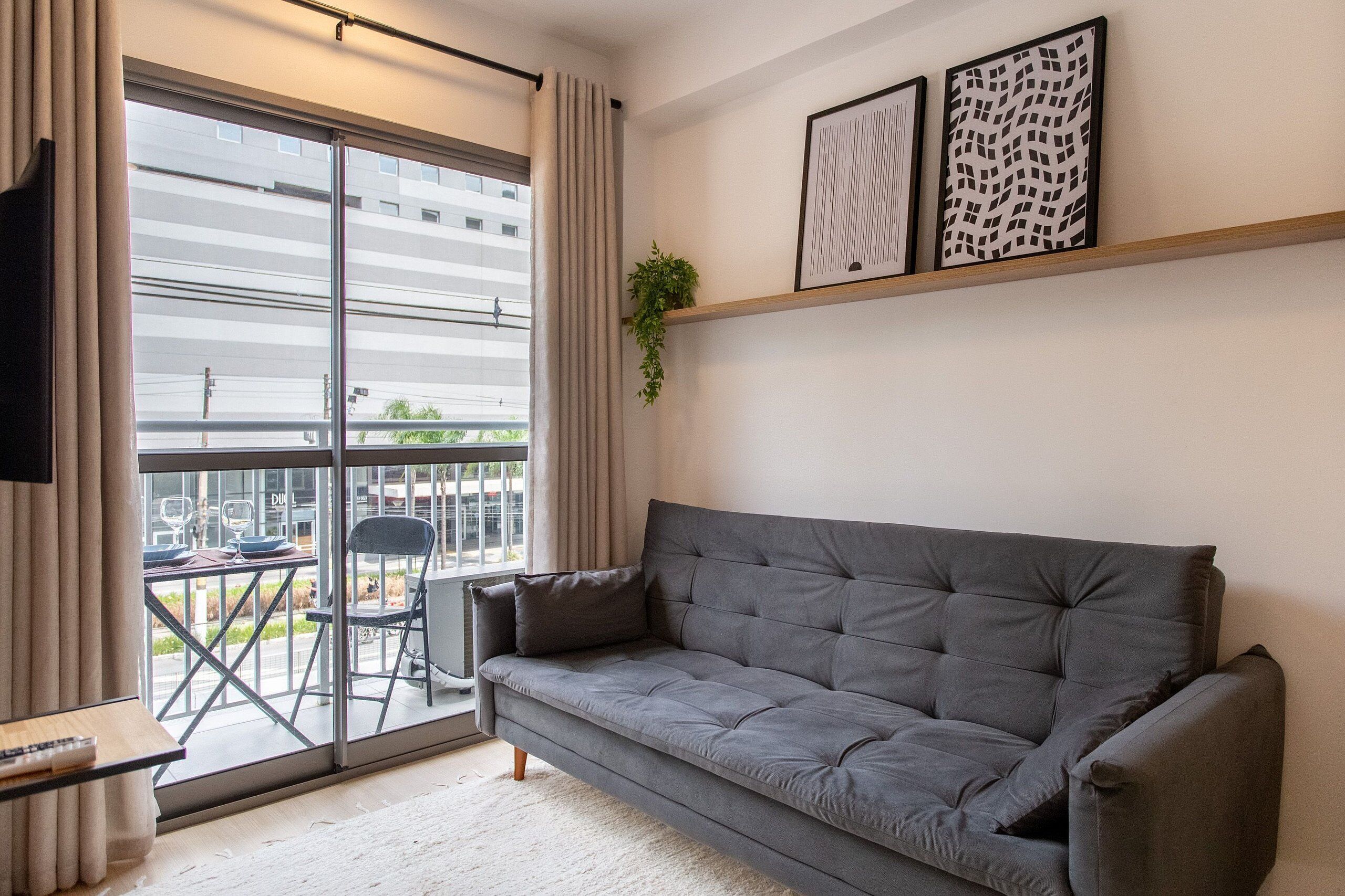 Un salon moderne avec un canapé gris, une petite table et une grande fenêtre avec des rideaux.