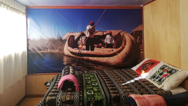 A room with a large mural of a boat on water, a bed with patterned bedding, and a window with curtains. - Room-lucsay Habitacion Vista Al Amanecer (Puno)