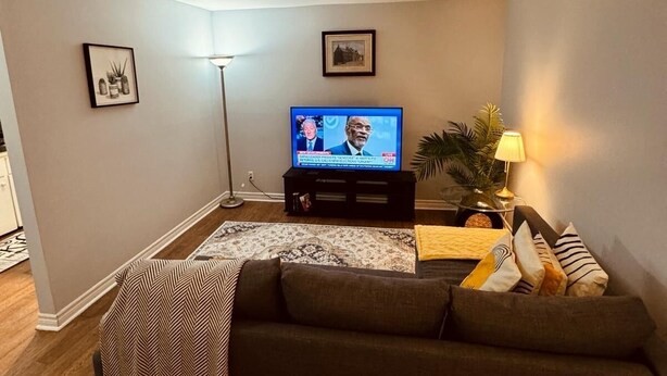 A living room with a sofa, a television, a floor lamp, and a small table with a lamp.