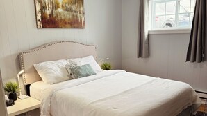 A bedroom with a large bed, a nightstand, a wall-mounted painting, a window with curtains, and a ceiling light.