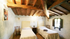 Een kamer met twee bedden, houten balken, een klein tafeltje met een lamp en een raam met gordijnen.
