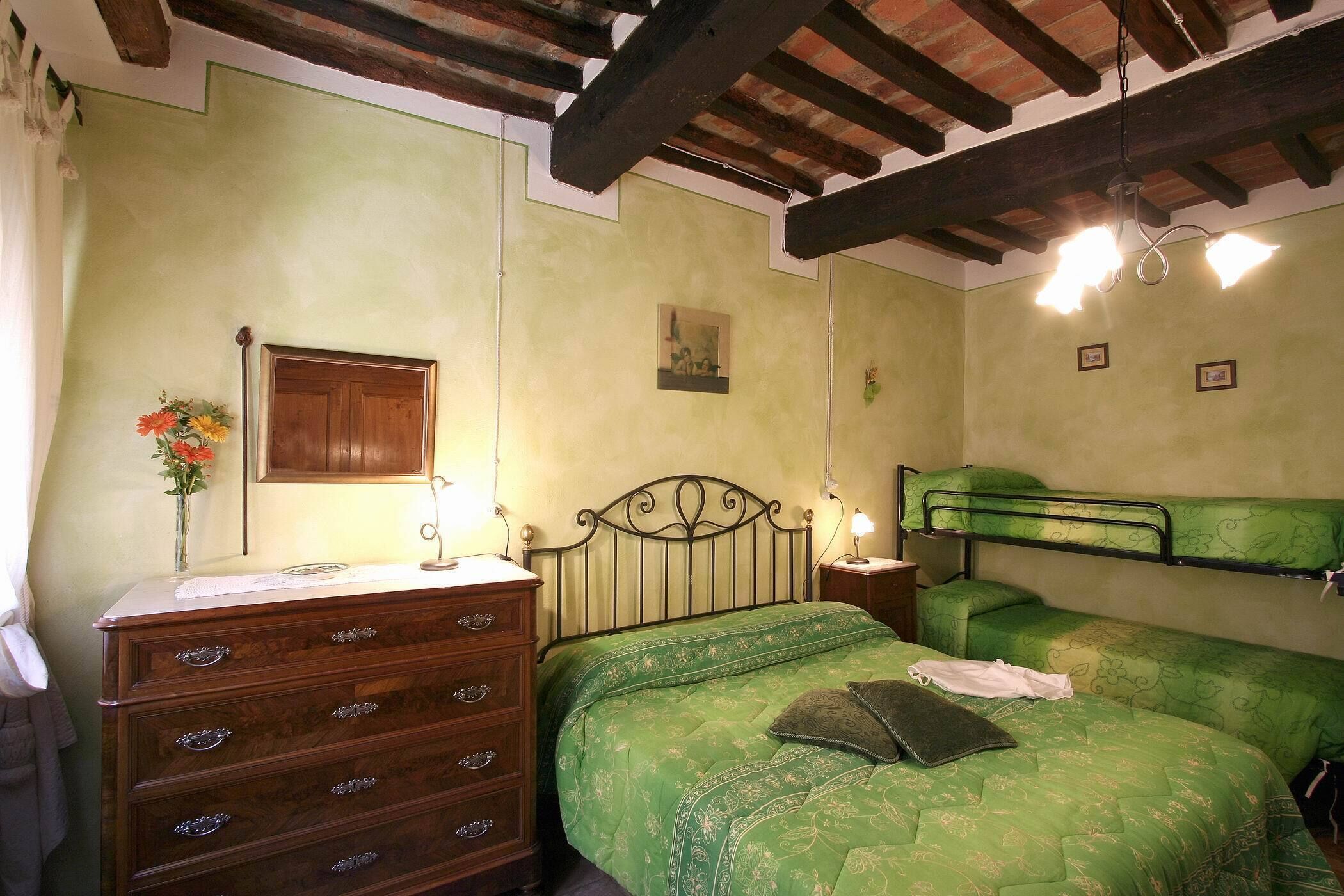 Ein Zimmer mit einem Holzkoffer, einem Bett mit grüner Bettwäsche, einem hölzernen Kopfteil und einer Decke mit freiliegenden Balken.