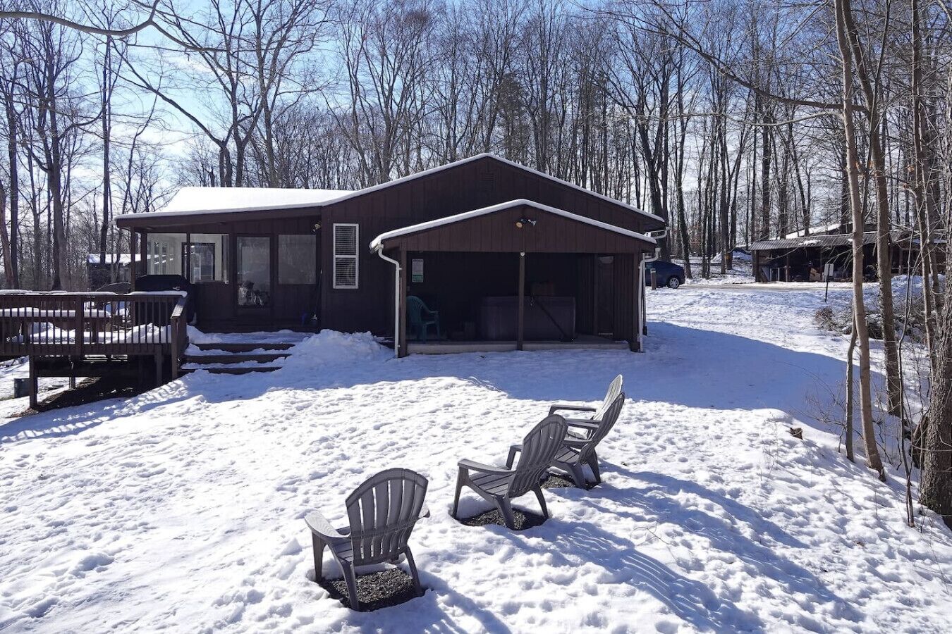 A cabin with a covered porch, two Adirondack chairs, and a bench.