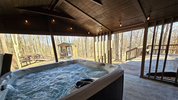 A hot tub in a covered outdoor area with a view of trees and a wooden deck.