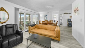 A living room with a black leather sofa, a mustard-colored sofa, and a coffee table. There is a dining area with a wooden table and chairs.