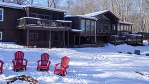 A lodge with a large deck and multiple windows, surrounded by snow-covered ground and trees.