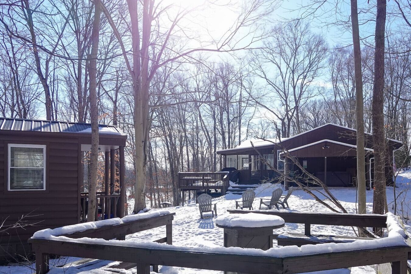 A cabin with a deck, a covered area, and a snow-covered ground.