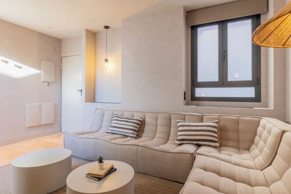 A modern living room with a sectional sofa, a round coffee table, and a large window with blinds.