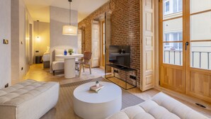 A modern living room with a brick wall, a flat-screen TV, and a cozy seating area. - Rio by Wynwood House (Madrid)