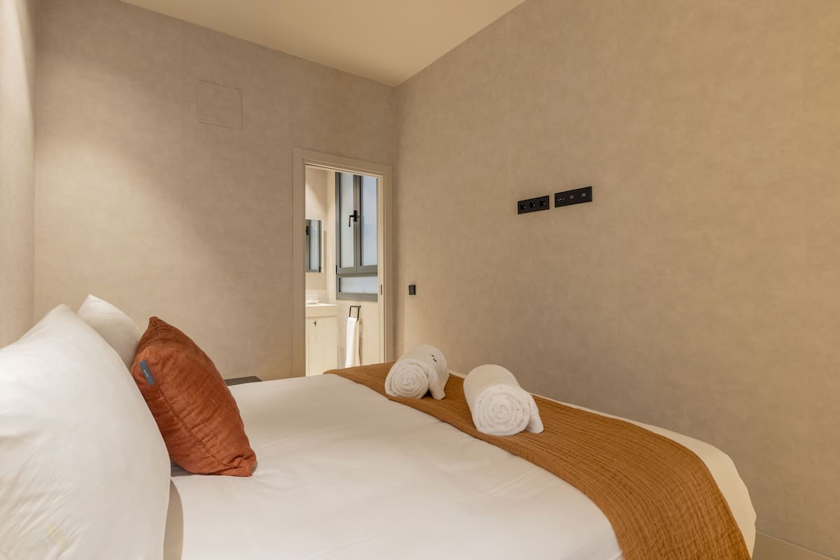 A hotel room with a bed, two pillows, a wooden headboard, and two rolled towels.