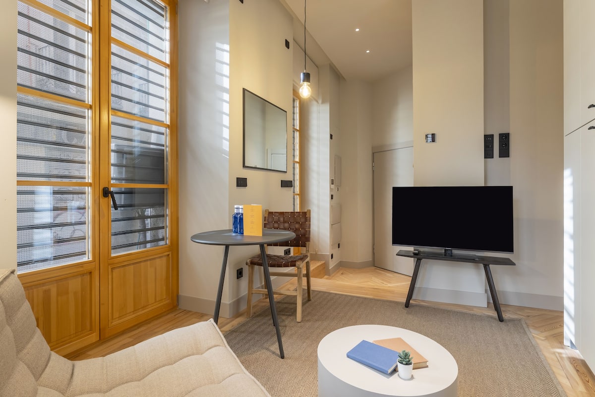 A modern living room with a sofa, a coffee table, a TV, and a window with blinds.