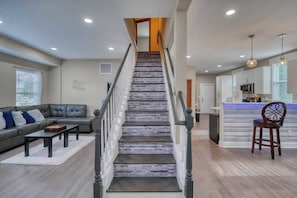 A staircase leading to a second floor, a living room with a sofa and coffee table, and a kitchen area with a microwave.