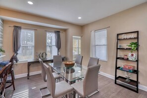 A dining area with a glass-top table, multiple chairs, and a black bookshelf with decorative items.