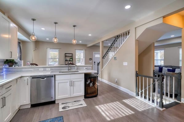 A modern kitchen with a central island, stainless steel appliances, pendant lighting, and a staircase leading to a living area.