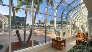 A spacious indoor area with large windows overlooking a pool and palm trees. - Cocoa Beach 2 BR 2 Bath Condo Ocean View & Balcony (Cocoa Beach)