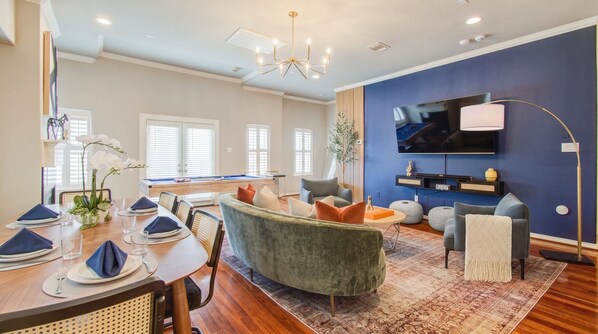 Living room with a curved velvet sofa, arc floor lamp and olive tree, seen from the dining table