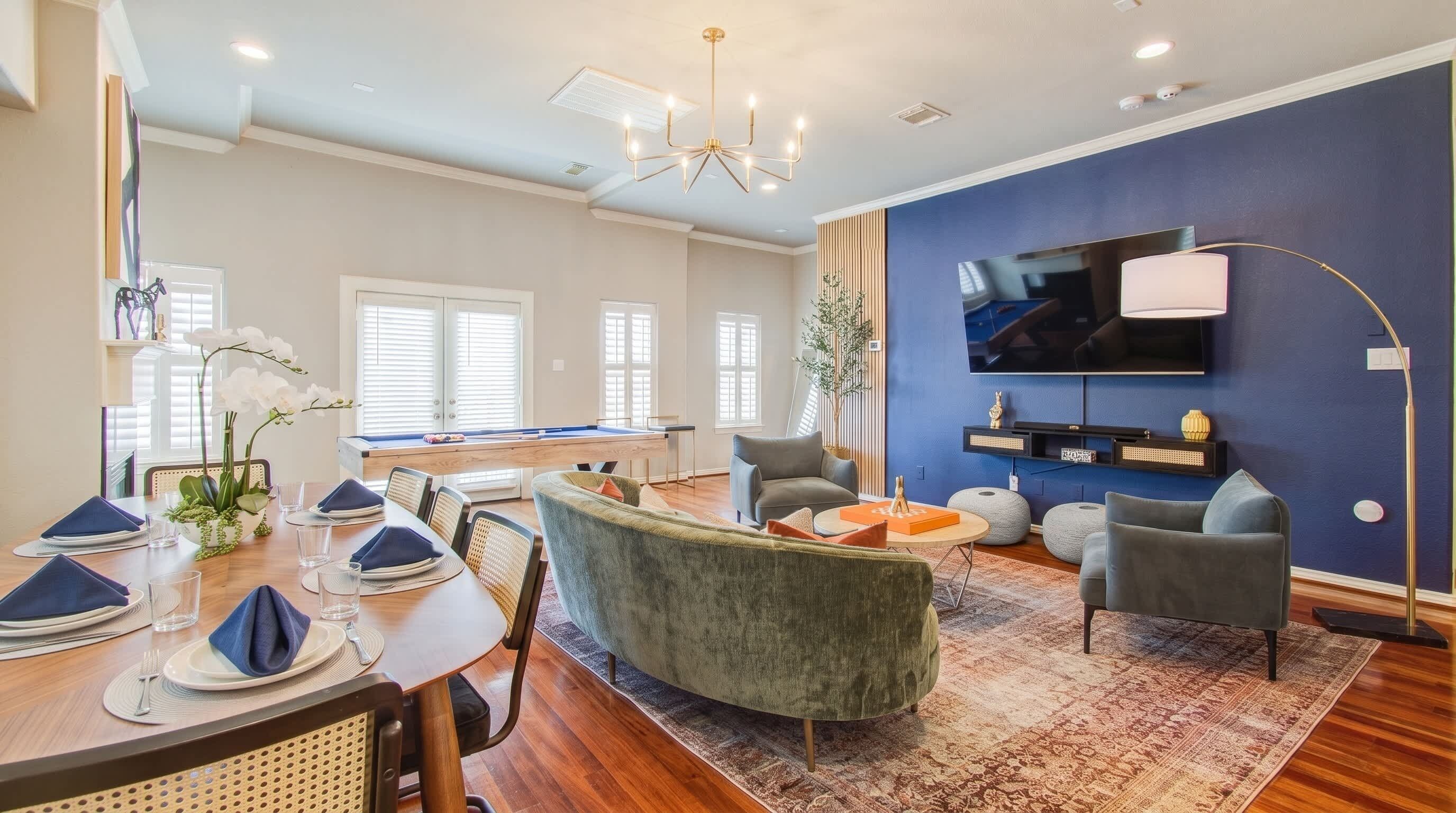 A modern living room with a pool table, comfortable seating, a flat-screen TV, and a dining area with a table set for four.