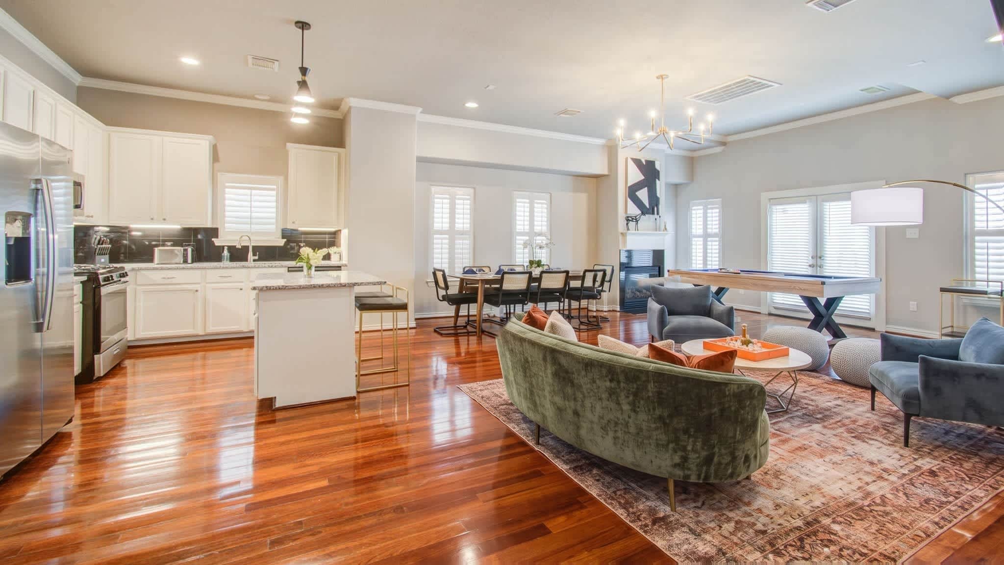 A spacious living area with a green sofa, a dining table with chairs, and a pool table.