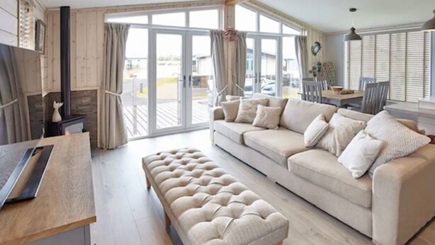 Un salon spacieux avec un canapé beige, un pouf assorti et une table basse en bois. De grandes portes vitrées donnent accès à un espace extérieur.