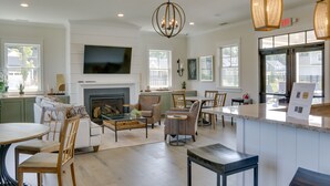A spacious living room with a fireplace, comfortable seating, a large TV, and a kitchen area with a countertop and dining space. - Beach House w/ Deck & Pool Access in Rehoboth (Rehoboth Beach)