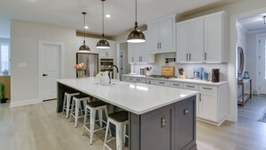 A modern kitchen with a large island, bar stools, pendant lighting, and white cabinetry. - Beach House w/ Deck & Pool Access in Rehoboth (Rehoboth Beach)