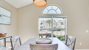 Un coin repas avec une table et des chaises en bois, un set de table en fibres naturelles, un panier posé sur le buffet, et une vue dégagée par une grande fenêtre.