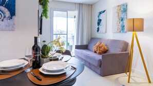 Un salon moderne avec un coin repas, comprenant un canapé, une table à manger avec de l’assiette et des couverts, une lampe et des œuvres d’art accrochées aux murs.