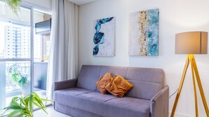 Un salon moderne avec un canapé gris, deux coussins, une lampe sur pied et des œuvres d’art abstraites accrochées au mur.