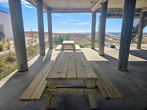 A wooden picnic table under a concrete structure with a view of the beach and distant landscape. - Boardwalk 1: Gulf-Front 4BR, Games, Pet Friendly (Pensacola)