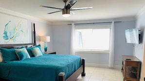 A bedroom with a bed, a ceiling fan, a TV, and a window with curtains.