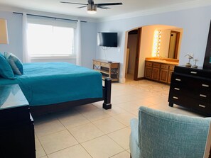 A bedroom with a bed, a desk, a chair, a TV, a vanity with lights, and a ceiling fan. - Boardwalk 1: Gulf-Front 4BR, Games, Pet Friendly (Pensacola)