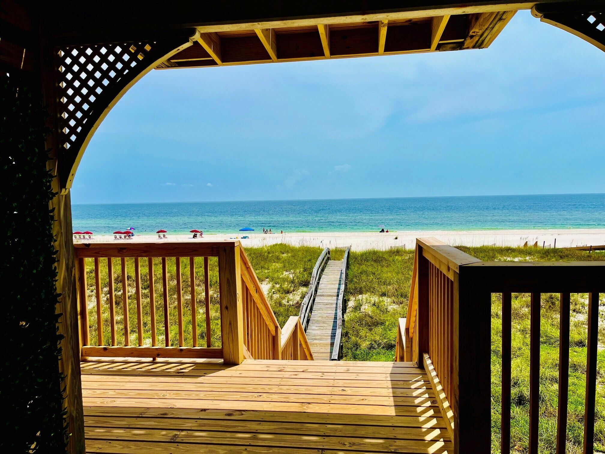 A wooden deck leading to a beach with a clear view of the ocean.