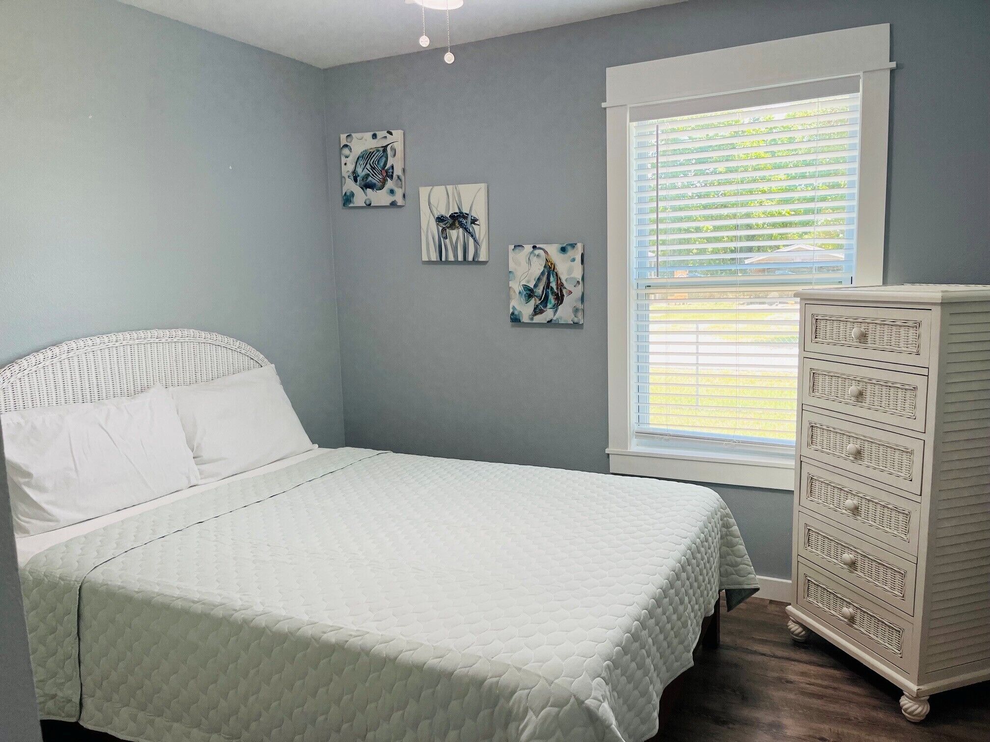 A bedroom with a bed, a dresser, and a window with blinds.